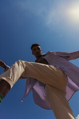 Fototapeta bottom view of african american man posing in trendy summer clothes under blue sunny sky obraz
