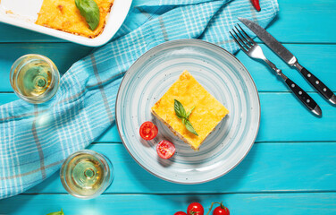 Delicious homemade italian Lasagna with bachamel sauce and glasses of wine on blue wooden background