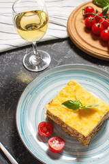 Delicious homemade italian Lasagna with bachamel sauce and glasses of wine on black stone background
