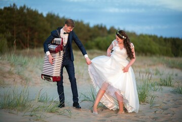 Beautiful shot of a young romantic bride and a groom with an accordion doing a funny pose