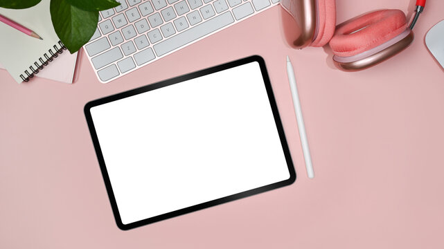 Flat lay digital tablet with white display, stylus pen, headphone, coffee cup and notebook on pink background