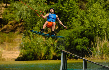 Fototapeta na wymiar Professional wakeboarder jumping over the water against the sky and trees