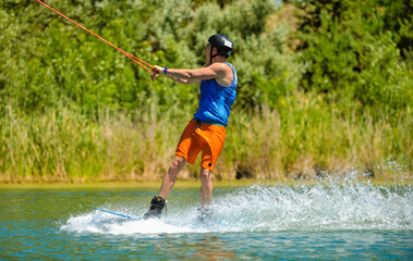 Fototapeta na wymiar A professional wakeboarder rides on the lake in sunny weather, performing figures