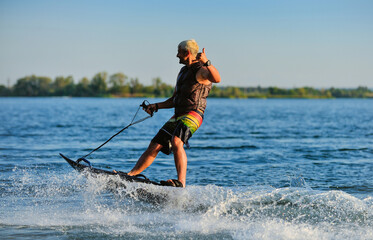 A professional wakeboarder rides on the lake in sunny weather, performing figures