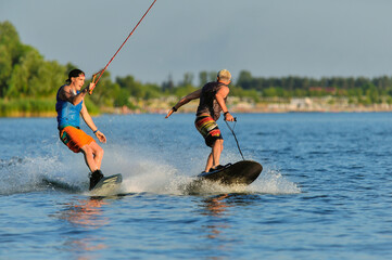 Professional wakeboarders ride on the lake in sunny weather with a good mood