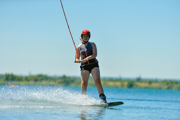 Beautiful girl wakeboarder rides on the lake in sunny weather