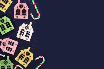 Christmas background with decorative, multicolored, wodden houses, sweets and golden confetti on a deep blue background with place for text. Merry Christmas composition, flat lay