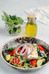 Greek salad on a plate. Vegetables, oil and cottage cheese on a table. Blurred background.