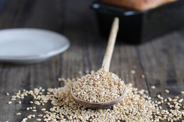 Wooden spoon filled with hard white wheat berries. Selective focus with blurred foreground and background. Loaf of bread in background.
