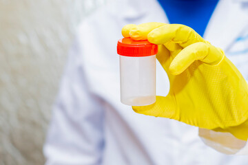 A doctor in a medical gown and protective gloves holds in his hand.empty container for analysis....
