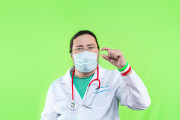 A doctor in a white coat and mask shows a small size with his fingers. Bracelet in the colors of the flag of Italy.