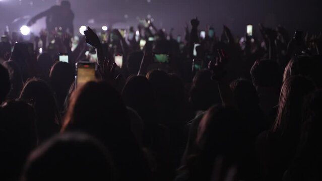 Unrecognizable fans dancing at a concert or festival party. Silhouettes of concert crowd in front of bright stage lights