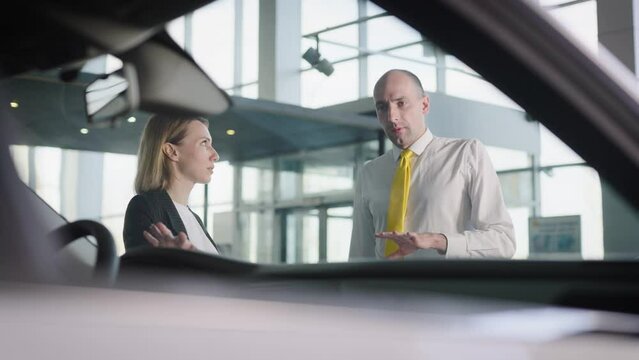Attractive woman picks up her car in a car dealership. Friendly seller, advises the client.