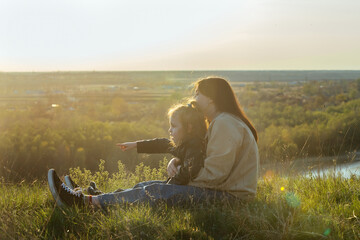 mother with her little daughter are sitting on the high bank of the river and admiring the view of...