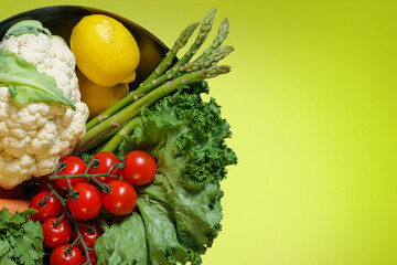 Bowl of fresh organic vegetables, salad, cauliflower, tomato, lemon, asparagus , carrot on yellow background with copy space, healthy food concept. High-quality photo