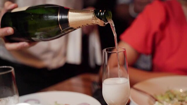 A waiter at the establishment pours sparkling wine into glasses to the girls sitting at the table during the celebration. Midplane in motion.