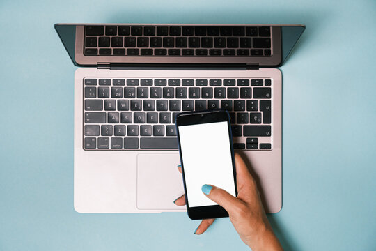 Top view of anonymous hand holding a smartphone with blank screen while using a computer
