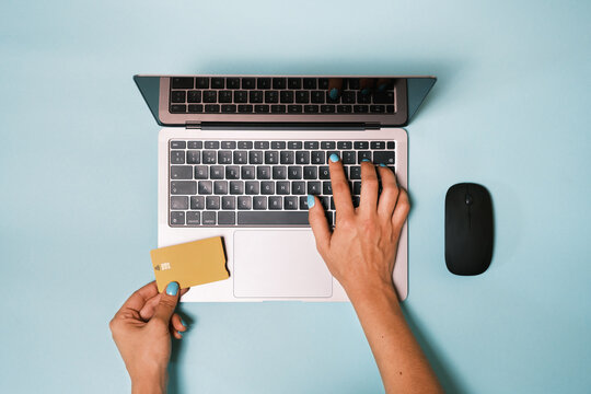 Top view of anonymous hand typing on the computer keyboard and holding a bank credit card while making an online payment