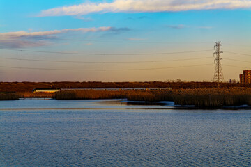 Obraz premium Railroad Tracks Against Sky During Sunset with blue sky, electric pylons line runs parallel to the railroad, view from water pond. High-quality photo