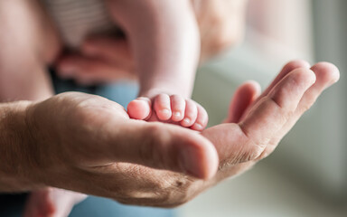 Close-up detail of parent holding cute and soft baby small leg in his hands. Macro abstract view of sweet baby foot fingers. Soft child skin feet. Love and family emotion