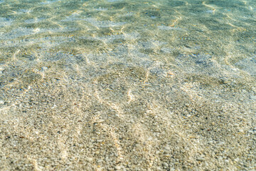 Close up photo of clear sea with pebbles and ripples.