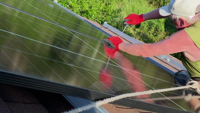 Worker fasten bolt installing solar panels on bituminous tiles roofing. DIY concept green energy