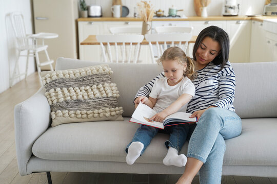 Mother, preschool daughter reading book together, enjoy family hobby at home. Parenting, motherhood.