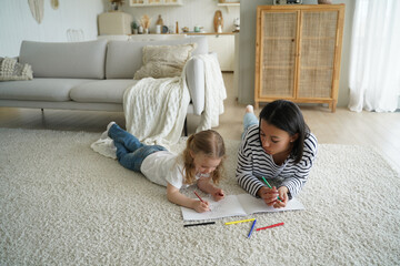Mother, little daughter paint together lying on floor in living room. Child creativity, parenting