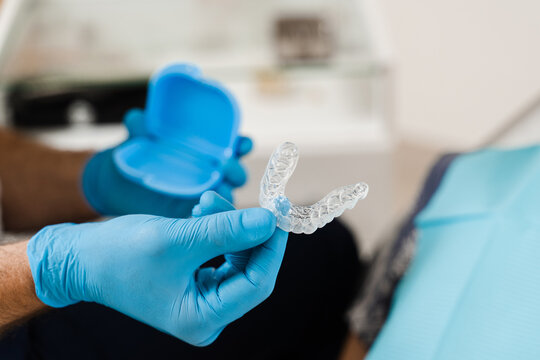 Clear aligner for bite correction and shape of teeth close-up. Orthodontist shows transparent removable retainer for patient woman in dentistry.