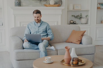 Young office worker working from home while sitting on couch with crossed leg