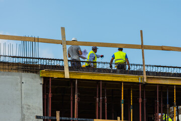 Fototapeta premium Three workers and a contractor on top of a construction site along with an engineer pointing to something