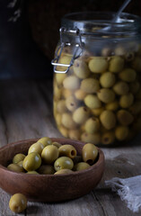 Green olives in a wooden bowl and glass jar