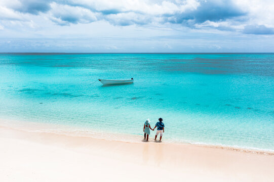 Man and woman holding hands on a tropical beach admiring the crystal clear sea, aerial view, Antigua and Barbuda, West Indies, Caribbean