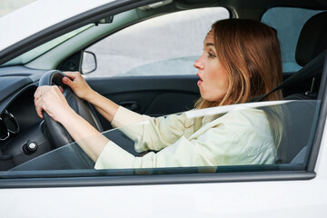 Scared business woman is looking on road front car. Woman driver driving her car, side view