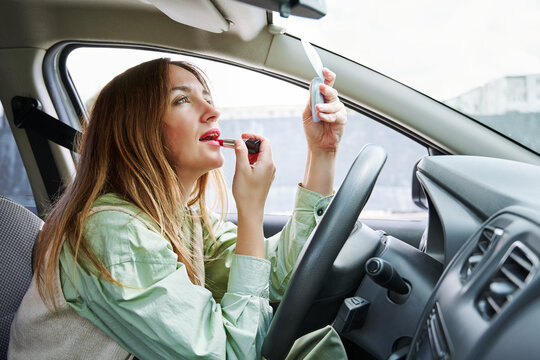 Young attractive woman holds red lipstick and paints her lips sitting at the wheel of a car
