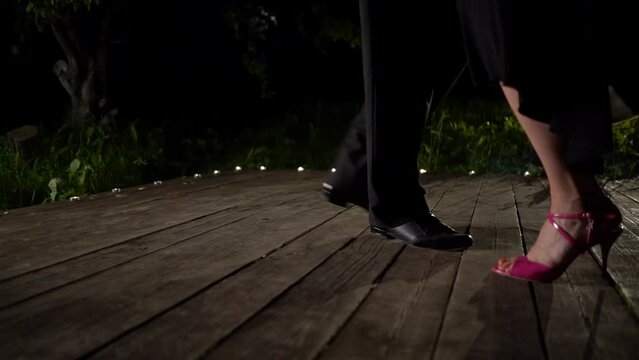 Closeup dancers legs performing latin dance on wooden support. Unknown couple feet dancing tango in dark background. Backlight