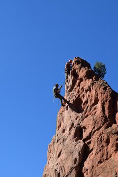 Vertical View Of Men Climbing A Big Red Rock On A Clear Sunny Day In Colorado Springs, CO