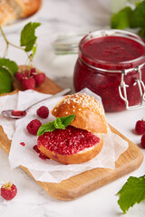 Bun with sesame seeds and raspberry jam. Jar with delicious homemade raspberry confiture. 