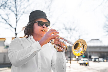 Young European or American male musician jazzman with long hair in white shirt, hat and sunglasses...