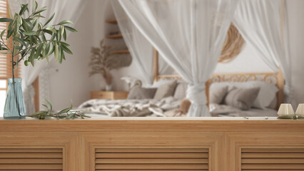 Fototapeta na wymiar Wooden table top, cabinet, panel or shelf with shutters close up. Olive branch in vase and candles. Blurred background with bohemian bedroom with canopy bed, boho style