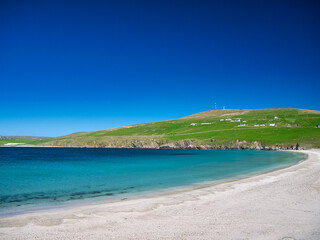 The white sand and turquoise water of Spiggie Beach (Scousburgh Beach) in southern Shetland, UK. Taken on a sunny day with a clear blue sky.