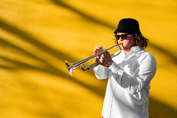 Young caucasian long-haired man in white shirt, hat and sunglasses playing funky jazz on silver...