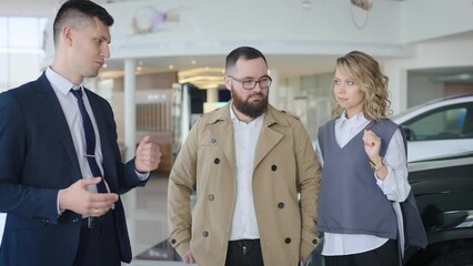 Sales manager in a car dealership serves a married couple. A man and a woman choose a new car - Powered by Adobe