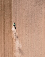 Vertical drone shot of a tractor working in the field and making dust