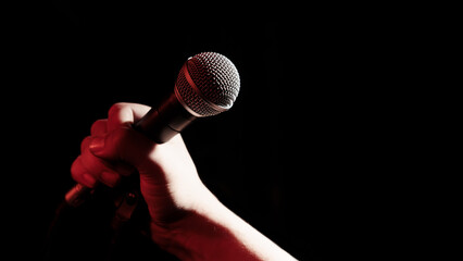 A man's hand holds a professional microphone on a black background