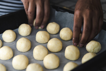 Latin woman placing rolls of chipa in the baking pan, traditional small cheese-flavored rolls