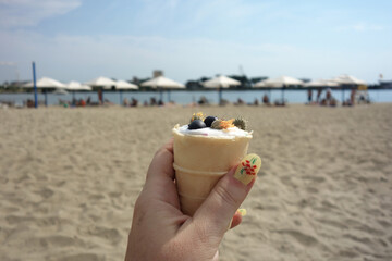 iceacream decorated with fruits on a beach with human hand