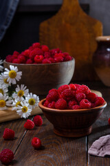 Fresh raspberries in a clay and wooden bowl on a dark wooden table
