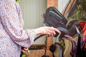 Mature woman using electric charging point at home to fuel electric car