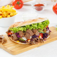 Döner Kebab Doner Kebap fast food meal in flatbread with fries on a kitchen board square